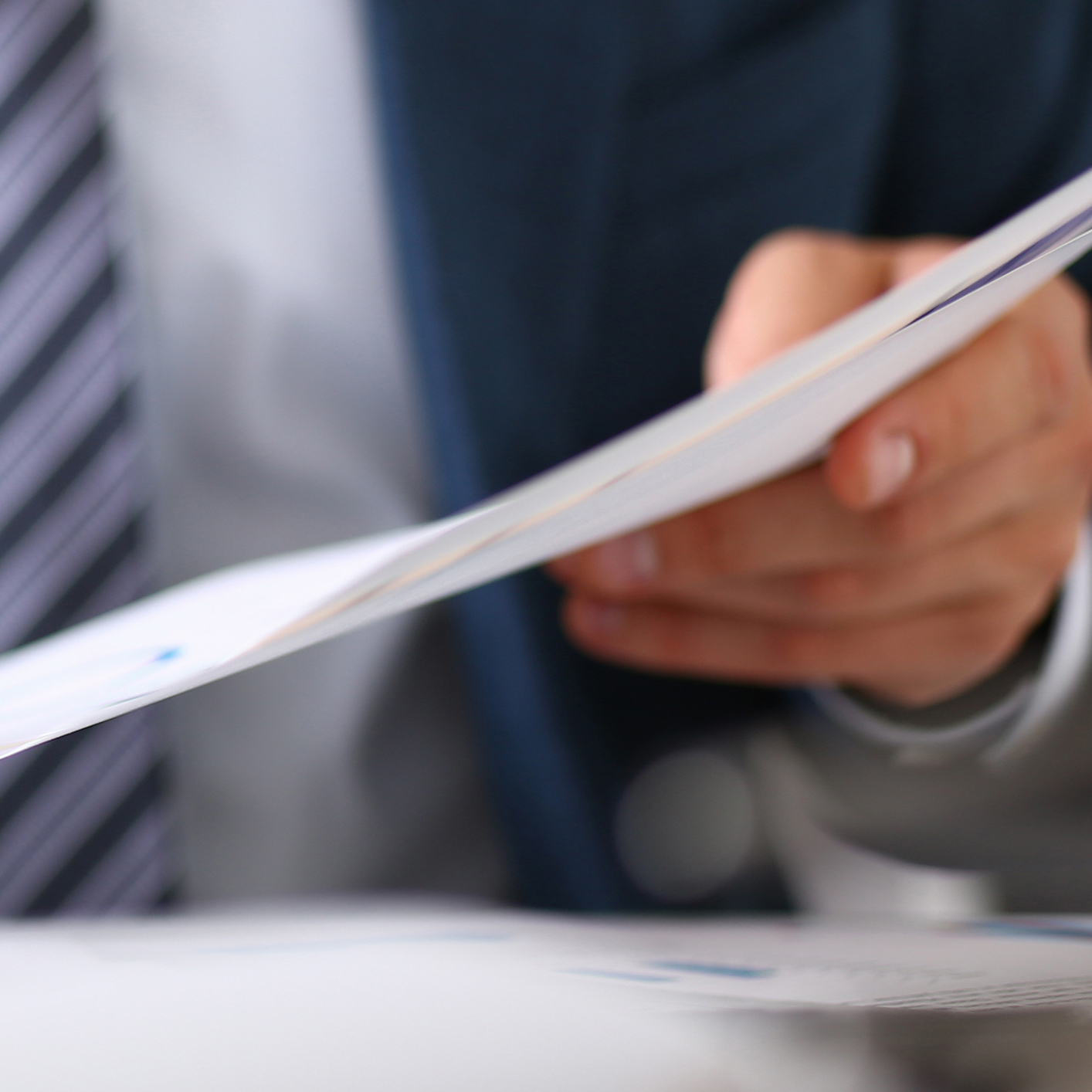 A person in a suit holds and reviews a stack of documents, with focus on their hand and the papers—reflecting the meticulous attention chicago lawyers bring to intellectual property law.