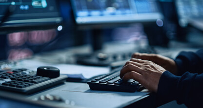 Person typing on a keyboard at a workstation with multiple computer monitors and control panels, providing litigation support services often used in law offices specializing in intellectual property law.