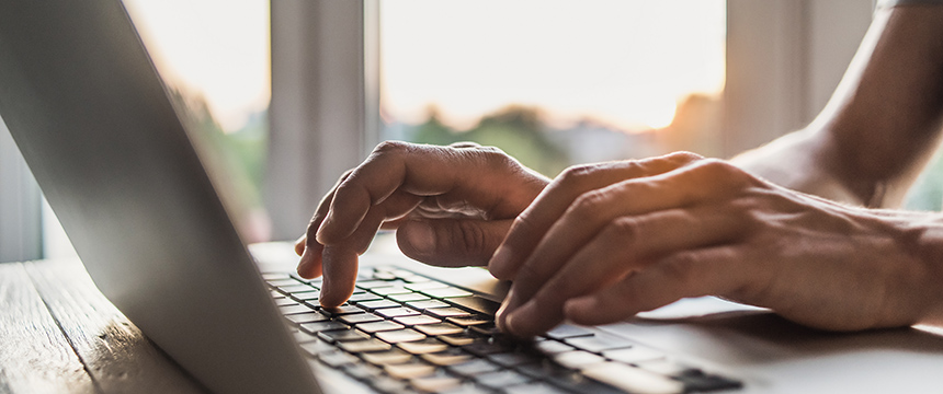 Hands typing on a laptop keyboard in a corporate law office, with natural light coming through a window—capturing the daily work of lawyers in Chicago.