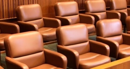 A row of empty brown leather chairs arranged in two tiers in a wooden jury box inside a courtroom, evoking the professional atmosphere found in a corporate law office or among top lawyers in Chicago.