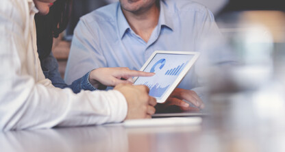 Two people review data charts on a tablet while seated at a table in a law office, with a third person in the background—all dressed in business attire, reflecting the professionalism of lawyers in Chicago.