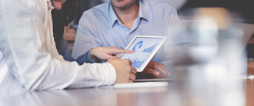 Two people review data charts on a tablet while seated at a table in a law office, with a third person in the background—all dressed in business attire, reflecting the professionalism of lawyers in Chicago.