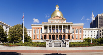 The Massachusetts State House in Boston, featuring a gold dome, red brick facade, columns, and two flags at the entrance under a clear blue sky, stands as an iconic symbol for the region’s corporate law office and intellectual property law professionals.