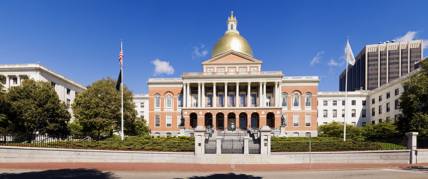 The Massachusetts State House in Boston, featuring a gold dome, red brick facade, columns, and two flags at the entrance under a clear blue sky, stands as an iconic symbol for the region’s corporate law office and intellectual property law professionals.