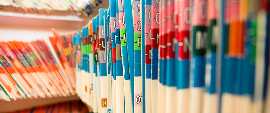 Rows of brightly colored file folders with lettered tabs are organized upright on shelves, commonly used for storing documents such as medical or office records in a corporate law office.