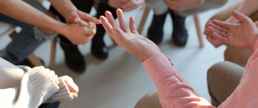 A group of people sitting in a circle, engaged in discussion at a corporate law office, with focus on hands gesturing while talking.