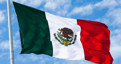 The national flag of Mexico, with green, white, and red vertical stripes and an eagle holding a snake on a cactus in the center, waves against a blue sky—symbolic in many chicago lawyers' offices specializing in corporate law.
