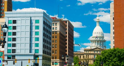 A city street with modern and historic buildings, including a white-domed capitol building in the background under a blue sky with clouds—home to top Chicago lawyers and corporate law offices.