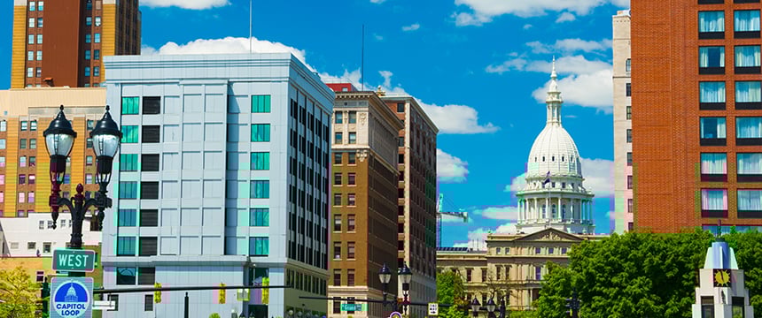 A city street with modern and historic buildings, including a white-domed capitol building in the background under a blue sky with clouds—home to top Chicago lawyers and corporate law offices.