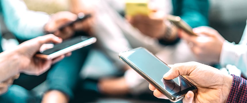 Several people sit close together, each holding and using a smartphone, with their hands and devices in focus—perhaps discussing matters related to intellectual property law or connecting with lawyers in Chicago.