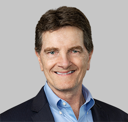 Smiling middle-aged man with short brown hair, wearing a blue dress shirt and dark blazer, posed against a plain light gray background, representing one of the top lawyers in Chicago at a renowned corporate law office.