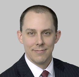 Man in a dark pinstripe suit, white shirt, and red tie, with short brown hair, facing the camera and smiling slightly—portraying the professionalism found in a corporate law office or among top lawyers in Chicago against a plain gray background.