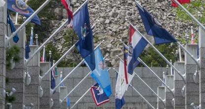 A stone memorial archway with multiple U.S. state flags displayed, flanked by trees on both sides, evokes the integrity and tradition found in a corporate law office dedicated to intellectual property law.