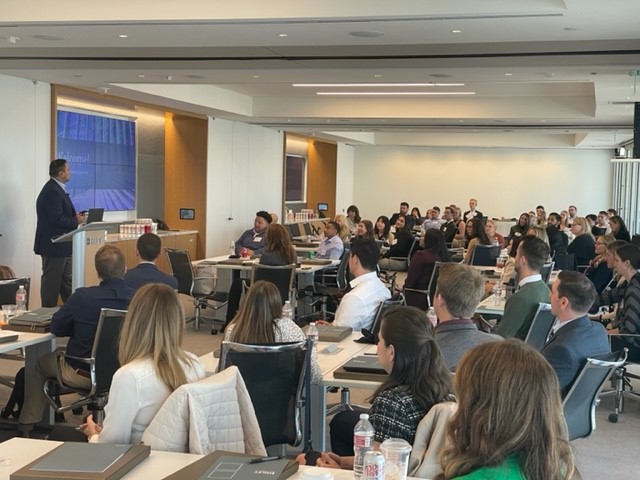 A speaker addresses a large group of chicago lawyers seated in a modern conference room with presentation screens and tables.