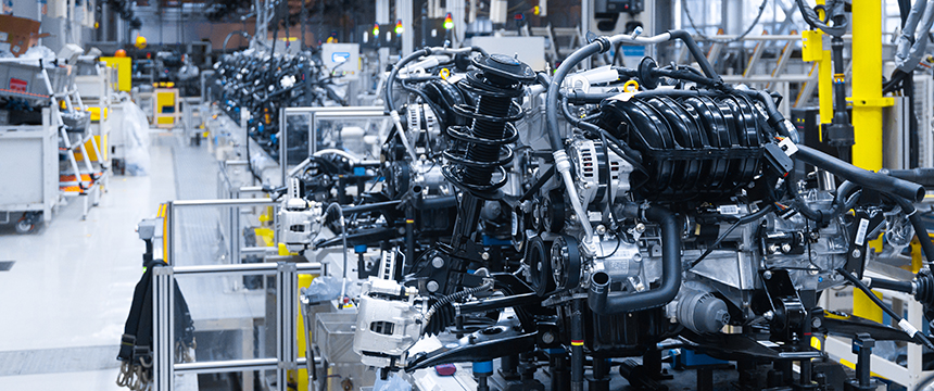 Automobile engines and parts move along an assembly line in a brightly lit, organized factory setting—protected innovations that might benefit from intellectual property law expertise.