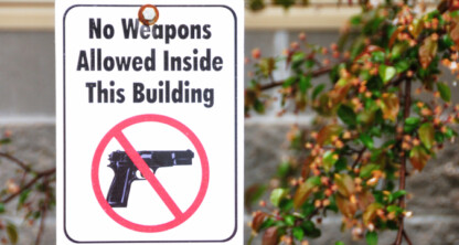 A sign at this corporate law office reads "No Weapons Allowed Inside This Building," with a crossed-out handgun image, indicating that firearms are prohibited for lawyers in Chicago and visitors alike.
