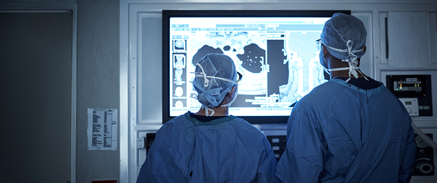 Two surgeons in scrubs and caps view medical scans on a large monitor in an operating room, collaborating much like lawyers in Chicago offering litigation support for complex intellectual property law cases.