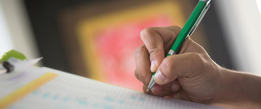A person holds a green pen and writes on a sheet of paper with printed text and numbers, possibly preparing documents for a corporate law office or litigation support.