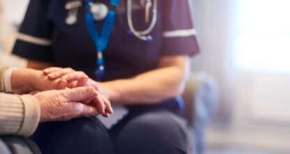 A healthcare professional in uniform holds the hands of an elderly person, providing comfort and support—much like litigation support assists clients in challenging times—in a well-lit indoor setting.