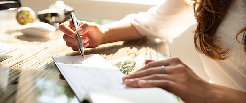 A person writes on a check with a pen while sitting at a desk in a corporate law office, highlighting the daily tasks handled by Chicago lawyers.