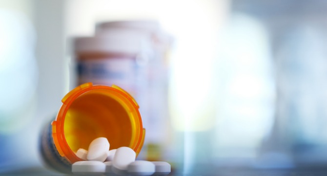 An orange prescription pill bottle tipped over with white tablets spilling out, with more pill bottles blurred in the background—often seen in litigation support cases handled by lawyers in Chicago.