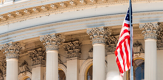 Close-up view of the United States Capitol building’s columns and an American flag in front, reflecting the prestige and authority that inspire top corporate law office professionals nationwide.