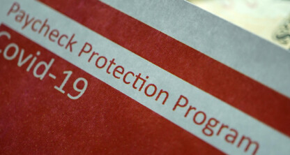 A close-up of a document labeled "Paycheck Protection Program Covid-19" with part of a US dollar bill visible in the background, ideal for use by lawyers in Chicago or a corporate law office offering litigation support.