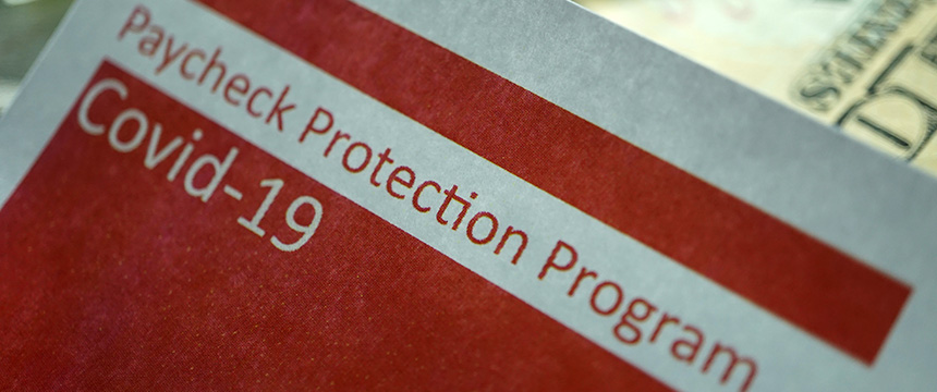 A close-up of a document labeled "Paycheck Protection Program Covid-19" with part of a US dollar bill visible in the background, ideal for use by lawyers in Chicago or a corporate law office offering litigation support.