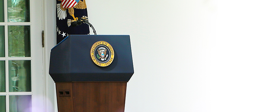 A podium with the Seal of the President of the United States stands outside near a glass door, with an American flag and eagle emblem in the background—reminiscent of a formal address at a prestigious corporate law office.