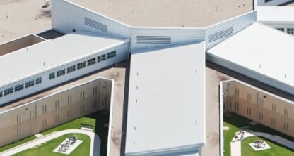 Aerial view of a large, modern correctional facility with multiple connected buildings and fenced outdoor areas, situated near corporate law offices.