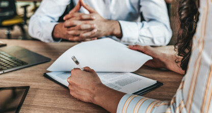Two people sit at a wooden desk with documents, a laptop, and a tablet; one person holds a pen and appears to be signing paperwork, suggesting the professional environment of law offices or lawyers in Chicago providing litigation support.