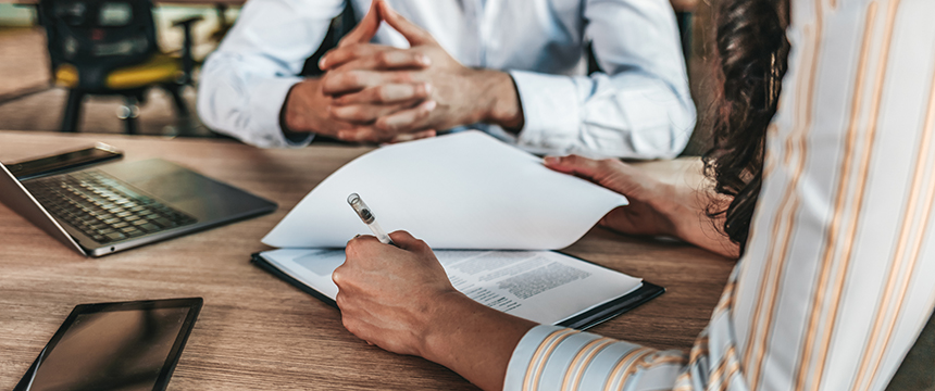 Two people sit at a wooden desk with documents, a laptop, and a tablet; one person holds a pen and appears to be signing paperwork, suggesting the professional environment of law offices or lawyers in Chicago providing litigation support.