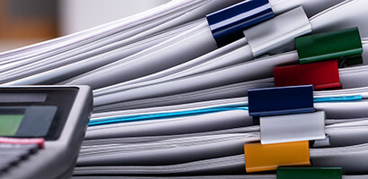 A close-up of a calculator next to several stacks of documents clipped with multicolored binder clips, often seen in law offices providing litigation support.