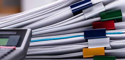 A close-up of a calculator next to several stacks of documents clipped with multicolored binder clips, often seen in law offices providing litigation support.