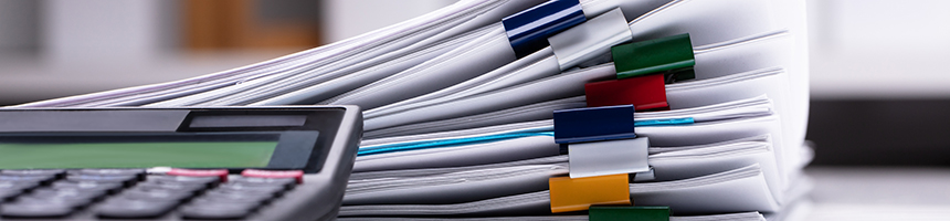A close-up of a calculator next to several stacks of documents clipped with multicolored binder clips, often seen in law offices providing litigation support.