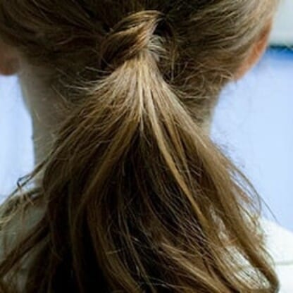 A person with brown hair tied in a ponytail sits facing a computer monitor in a bright indoor setting, typical of modern law offices.