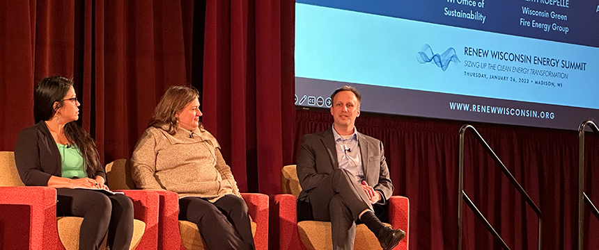 Three panelists sit on stage in armchairs at the RENEW Wisconsin Energy Summit, with a presentation screen and red curtain in the background, discussing how law offices can offer litigation support for clean energy initiatives.