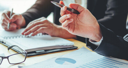 Two chicago lawyers in business attire review and discuss documents and charts at a desk, offering litigation support, with one holding a pen and notebook while eyeglasses rest on the table.