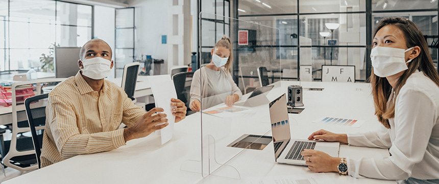 Three people wearing face masks sit at a conference table in a modern corporate law office, separated by clear dividers, with laptops and documents in front of them—reflecting the professionalism of Chicago lawyers.