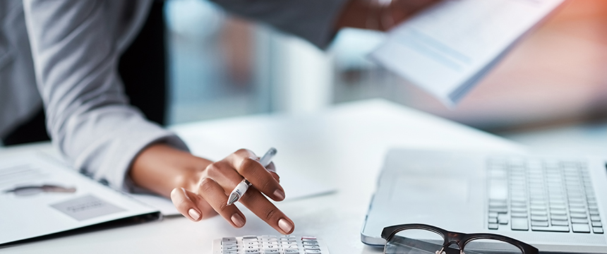 Person using a calculator and holding papers at a desk with a laptop and eyeglasses, reflecting the busy environment often found in Chicago lawyers' corporate law office settings.
