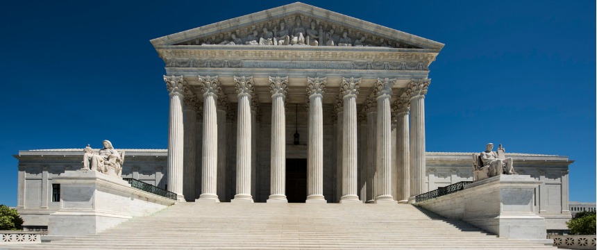 The front view of the United States Supreme Court building with tall columns, wide steps, and statues on both sides under a clear blue sky inspires law offices and litigation support teams nationwide.
