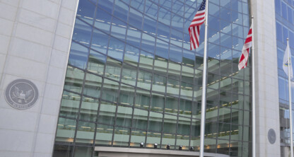 Modern glass facade of a government building with two flagpoles displaying the US and Washington D.C. flags, reminiscent of a corporate law office specializing in intellectual property law.