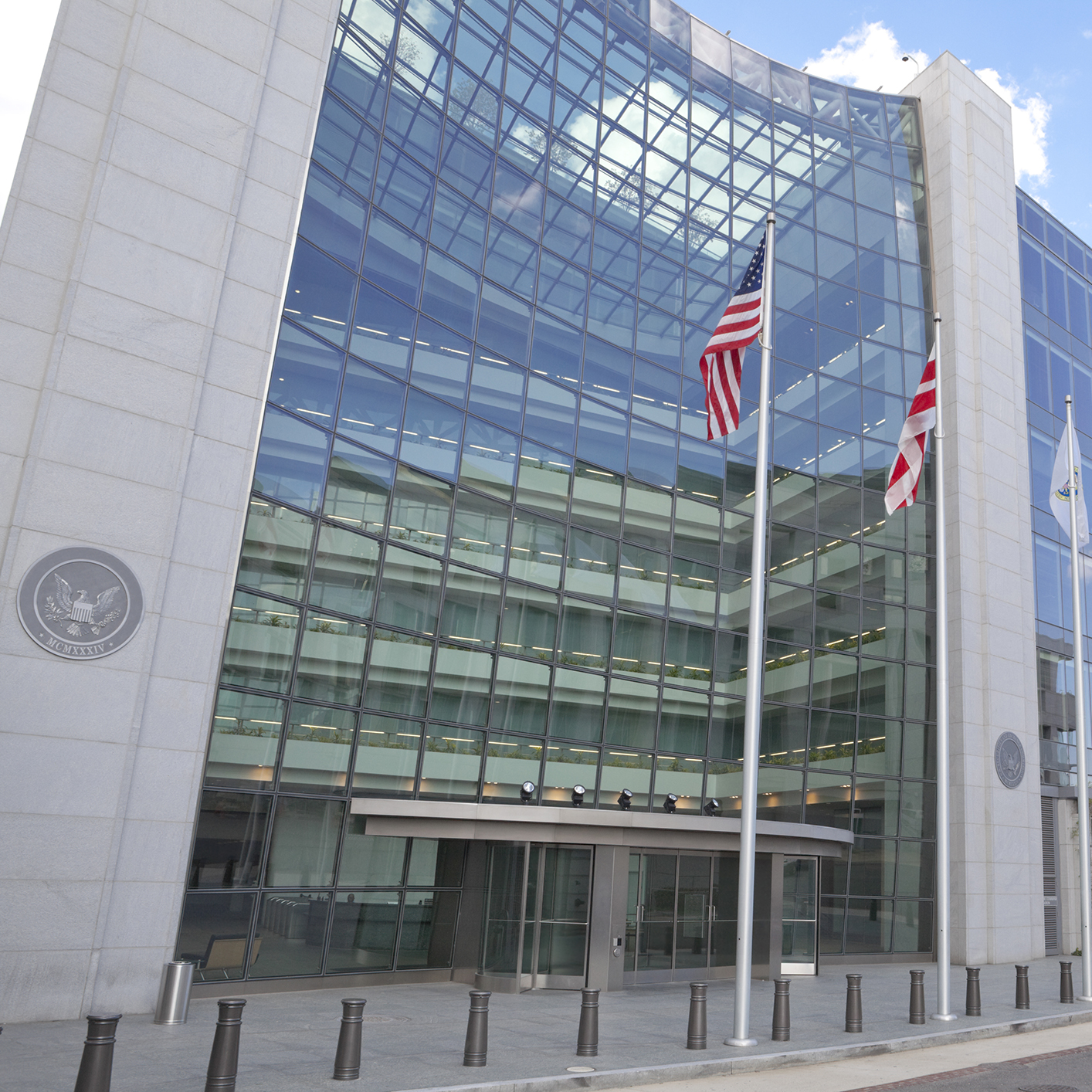 Modern glass facade of a government building with two flagpoles displaying the US and Washington D.C. flags, reminiscent of a corporate law office specializing in intellectual property law.