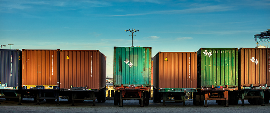 Several shipping containers in various colors are lined up on trailers in an outdoor industrial area under a clear blue sky, reminiscent of the bustling logistics often managed by Chicago lawyers at a nearby corporate law office.