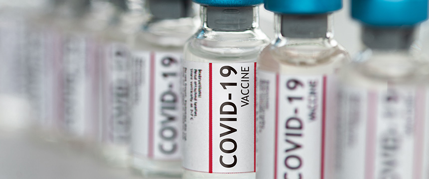Rows of clear vials labeled "COVID-19 Vaccine" with blue caps are arranged closely together, some in focus and others blurred in the background—mirroring the precision often found at Chicago lawyers’ offices.