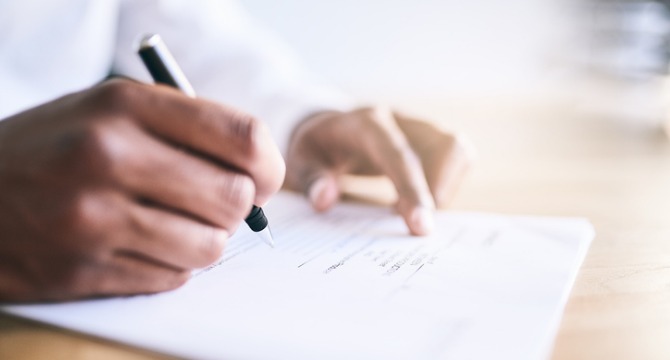 A person writes on a sheet of paper with a pen at a desk in one of the leading law offices, reflecting on matters related to intellectual property law.