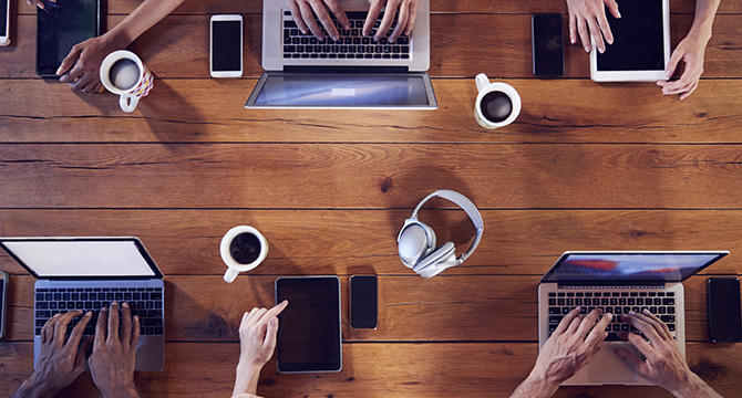 Top-down view of lawyers in Chicago working at a wooden table with laptops, tablets, smartphones, coffee cups, and headphones—collaborating on intellectual property law and litigation support cases.