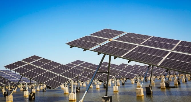 Rows of solar panels are installed above water, elevated on concrete supports under a clear blue sky—an innovative solution often discussed in law offices specializing in intellectual property law.