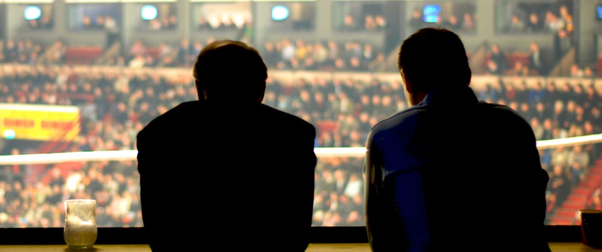 Two people sit side by side with their backs to the camera, overlooking a crowded indoor arena with a blurred audience—much like chicago lawyers surveying a busy courtroom from afar.