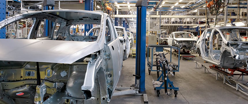 Partially assembled car bodies on an automotive production line in a factory, where efficiency rivals the precision of chicago lawyers offering litigation support. Machinery and equipment are visible throughout the scene.